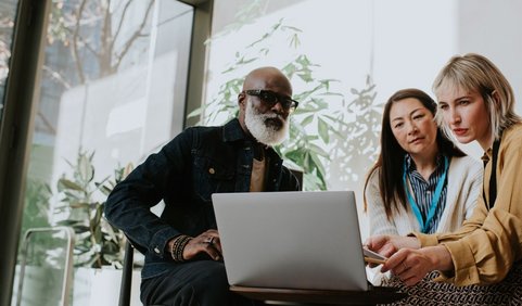 Three employees analyzing information together on a laptop.