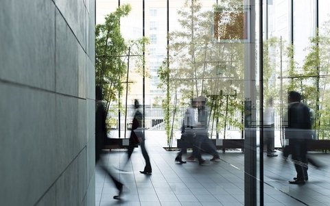 People walking through the glass-fronted lobby of a modern office building