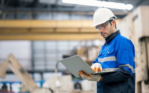 Occupational safety professional wearing a white helmet and blue jacket, using a laptop