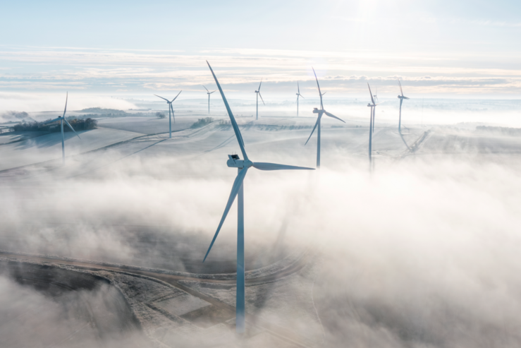 Aerial view of windmills rising above morning fog over green farmland