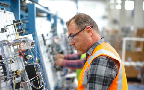 Technician wearing safety glasses and high-visibility vest inspecting electrical wiring on industrial equipment – Lockout Tagout safety procedures