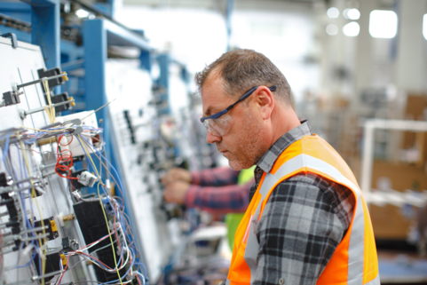 Technician wearing safety glasses and high-visibility vest inspecting electrical wiring on industrial equipment – Lockout Tagout safety procedures