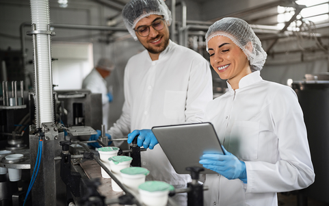 Quality inspector in hairnet and gloves using a tablet on a production floor